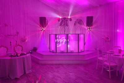 Salle de réception décorée avec éclairage rose, scène avec écran lumineux, chaises et tables élégantes.