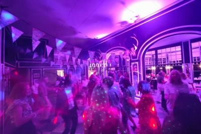 Des personnes dansent sous des lumières colorées dans une salle décorée avec des guirlandes et des arches.