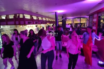 Des personnes dansent dans une salle éclairée par des lumières violettes, avec un décor intérieur moderne en arrière-plan.