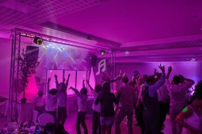 Des personnes dansent sous des lumières colorées dans une salle de fête avec un DJ sur une scène éclairée.