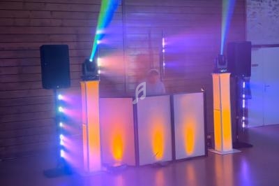 Un DJ mixe derrière une table éclairée par des lumières colorées dans une salle aux murs en bois.