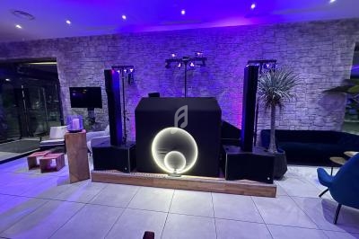 Console DJ lumineuse avec éclairage violet, entourée d'enceintes et située dans une salle au mur en pierre apparente.