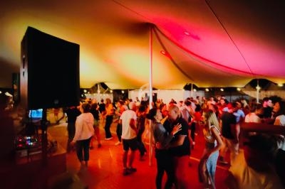 Des personnes dansent sous une grande tente éclairée de lumières colorées lors d'un événement festif en soirée.