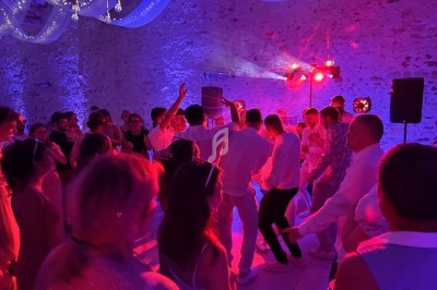 Groupe de personnes dansant sous des lumières colorées dans une salle en pierre décorée de voilages et guirlandes lumineuses.
