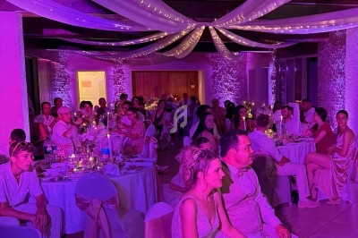 Des invités assis dans une salle de réception décorée de voilages et lumières violettes, lors d’un mariage.