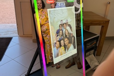 Un miroir photo interactif reflète un couple souriant et affiche une photo imprimée de groupe en bas.