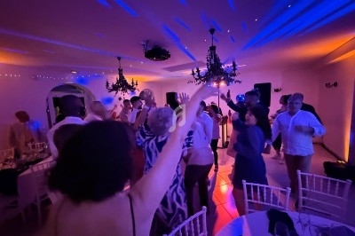 Des personnes dansent sous des lumières colorées dans une salle décorée avec des chandeliers suspendus.