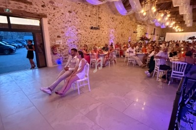 Salle de réception décorée avec des guirlandes lumineuses, des invités assis à des tables et un couple au premier plan.