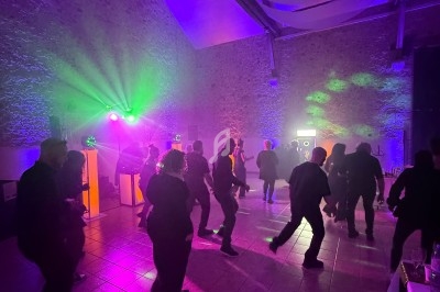 Personnes dansant dans une salle éclairée par des lumières colorées, avec un mur en pierre en arrière-plan.