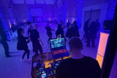 Un DJ mixe devant une piste de danse où des personnes profitent d'une ambiance lumineuse violette dans une salle en pierre.