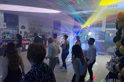 Personnes dansant dans une salle éclairée par des jeux de lumière colorés, avec des décorations et un bar en arrière-plan.