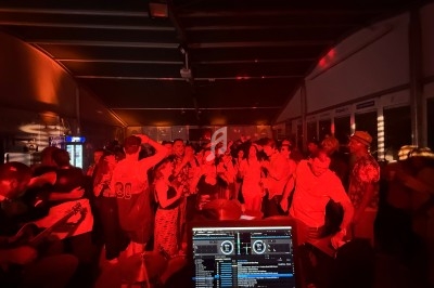 Groupe de personnes dansant dans une ambiance festive et lumineuse avec un DJ en arrière-plan.