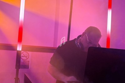 Un DJ mixant sur son ordinateur portable, entouré de lumières colorées et d'une ambiance enfumée.