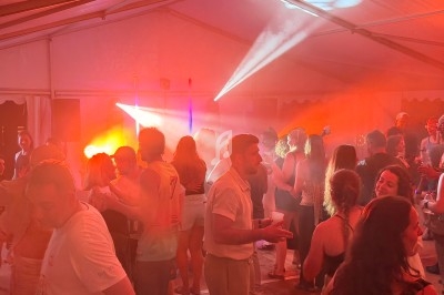 Groupe de personnes dans une tente éclairée par des lumières colorées, discutant et dansant lors d'un événement festif.