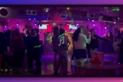 Des personnes dansent dans une salle de fête éclairée par des lumières colorées et des spots lumineux.