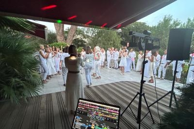 Groupe de personnes en tenue blanche dansant en extérieur, vu depuis une table de mixage sous un auvent.