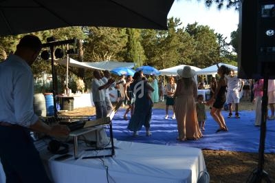 Groupe de personnes dansant en extérieur sur une piste bleue, entourées de tentes et d'arbres par temps ensoleillé.