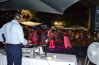 Un DJ mixe de la musique lors d'une fête en plein air, avec des invités dansant sous des lumières colorées.