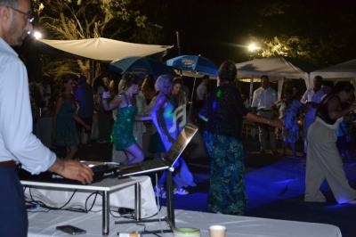 Des personnes dansent en soirée en plein air sous des lumières colorées, avec un DJ au premier plan.