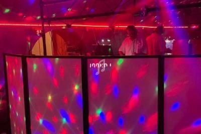 Des lumières colorées illuminent une cabine de DJ dans une ambiance de fête avec des personnes en arrière-plan.