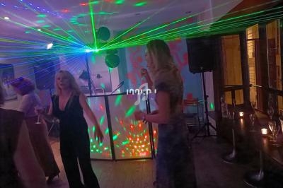 Des personnes dansent près d'une piste éclairée par des lasers colorés, avec un DJ en arrière-plan.