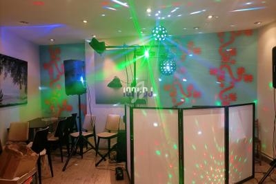 Installation de matériel de DJ avec jeux de lumières colorés dans une petite salle décorée de motifs rouges.