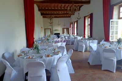 Salle de réception lumineuse avec tables rondes dressées, nappes blanches, chaises houssées et décorations florales.