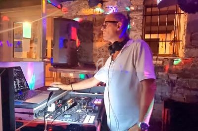 Un DJ mixe de la musique sur une table de mixage dans un lieu éclairé par des lumières colorées.