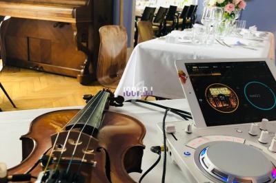 Un violon et une console DJ posés sur une table, avec un piano et une salle de réception en arrière-plan.