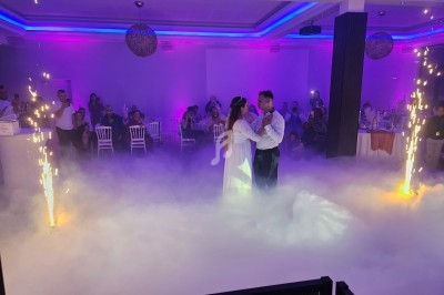 Un couple danse au centre d'une salle éclairée de lumières colorées, entouré de fumée et d'étincelles.