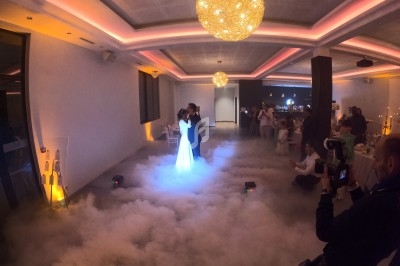 Un couple danse au centre d'une salle éclairée, entouré d'un effet de fumée au sol et de convives assis.