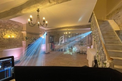 Salle de réception avec murs en pierre, tables dressées, éclairage tamisé et projecteurs lumineux près d'un escalier.
