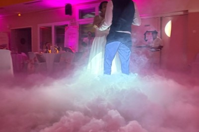 Un couple danse au milieu d'une piste enveloppée de fumée, éclairée par des lumières roses dans une salle de réception.