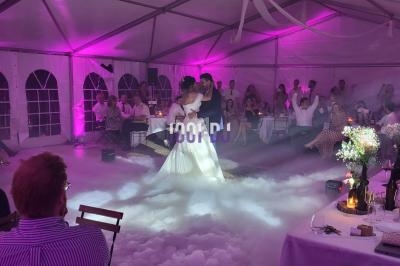 Un couple danse sous une tente éclairée de lumières roses, entouré d'invités assis et d'une ambiance de fumée au sol.
