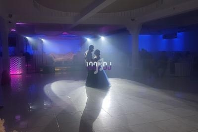 Un couple danse au centre d'une salle éclairée par des projecteurs, avec un canapé en arrière-plan.