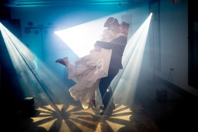 Un couple danse sous des projecteurs lumineux dans une salle sombre, l'homme portant la femme dans ses bras.
