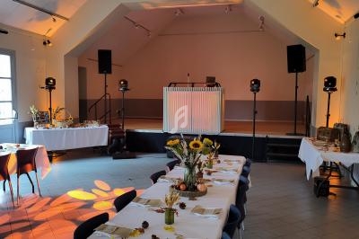 Salle décorée pour un événement avec tables dressées, fleurs de tournesol et espace DJ sur une petite scène.