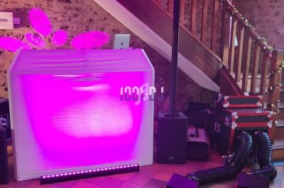 Stand de DJ éclairé en rose avec des enceintes, des équipements audio et un escalier en bois en arrière-plan.