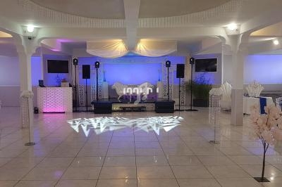 Salle de réception décorée avec des lumières colorées, une scène centrale et des tables dressées en arrière-plan.