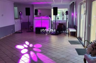 Salle de réception avec éclairage rose, piste de danse, matériel de sonorisation et décoration florale.