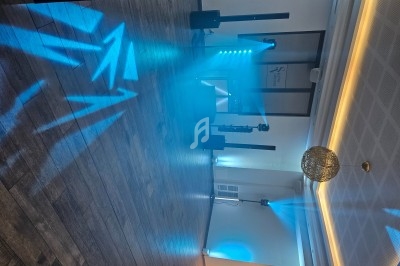 Salle de réception vide avec éclairage bleu et projecteurs, parquet en bois et décoration lumineuse suspendue.