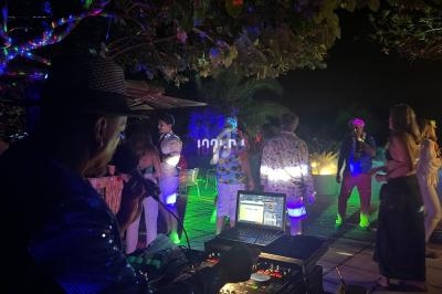 Un DJ mixe en plein air lors d'une soirée nocturne avec des invités dansant sous des lumières colorées.