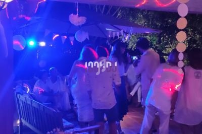 Groupe de personnes en tenue blanche dans une ambiance festive avec éclairages colorés, en extérieur de nuit.