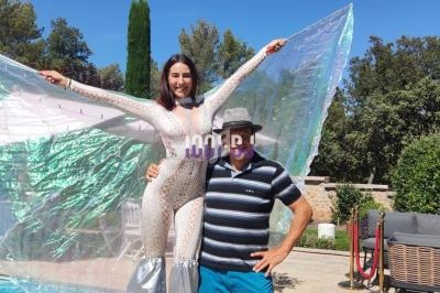 Une femme en costume scintillant pose sur des échasses à côté d'un homme près d'une piscine en plein air.