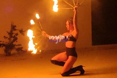 Une femme en tenue noire manipule des éventails enflammés dans un espace extérieur faiblement éclairé.