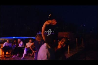 Personnes dansant en extérieur la nuit, éclairées par des lumières tamisées, avec des tables en arrière-plan.