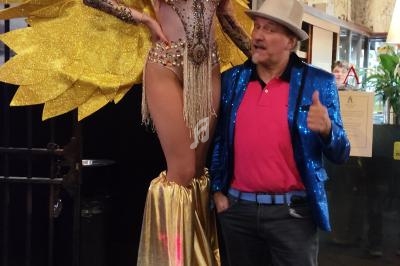 Une femme en costume doré avec des ailes et des échasses pose à côté d'un homme en tenue colorée.