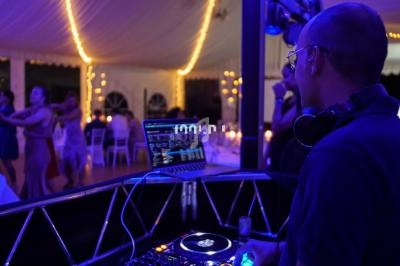 Un DJ mixe de la musique lors d'une soirée dansante sous une tente éclairée par des guirlandes lumineuses.