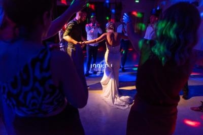 Des invités dansent autour d'une mariée en robe blanche sur une piste éclairée par des lumières colorées.