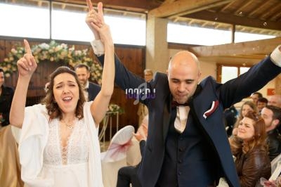 Un couple célèbre son mariage en levant les bras, entouré d'invités dans une salle décorée de fleurs.